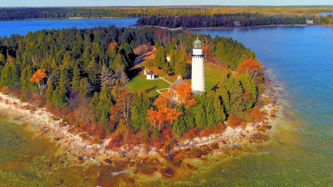 aerial view of a lighthouse in door county surrounded by fall trees on a rocky shoreline with blue lake water