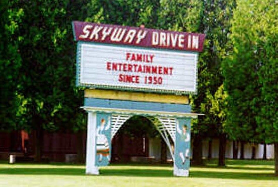 A tall sign for a drive in movie theatre on a lawn with trees behind