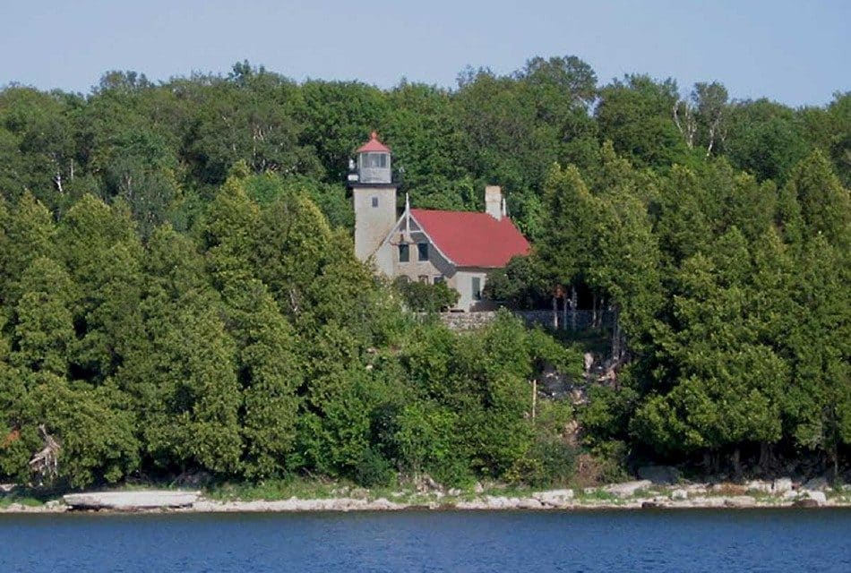 A historic lighthouse building nestled among a forest of trees next to a lake
