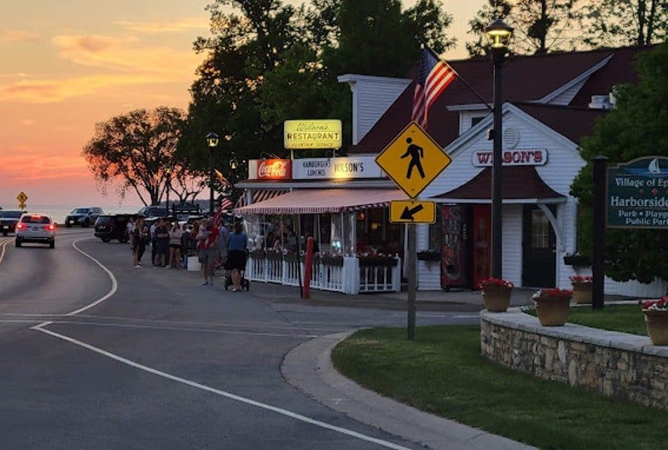 An ice cream shop at the corner of a winding road with people standing in line outside