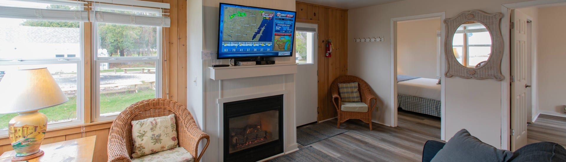 Interior of a cottage with living room, wicker chairs, gas fireplace wth TV and doorway into a bedroom