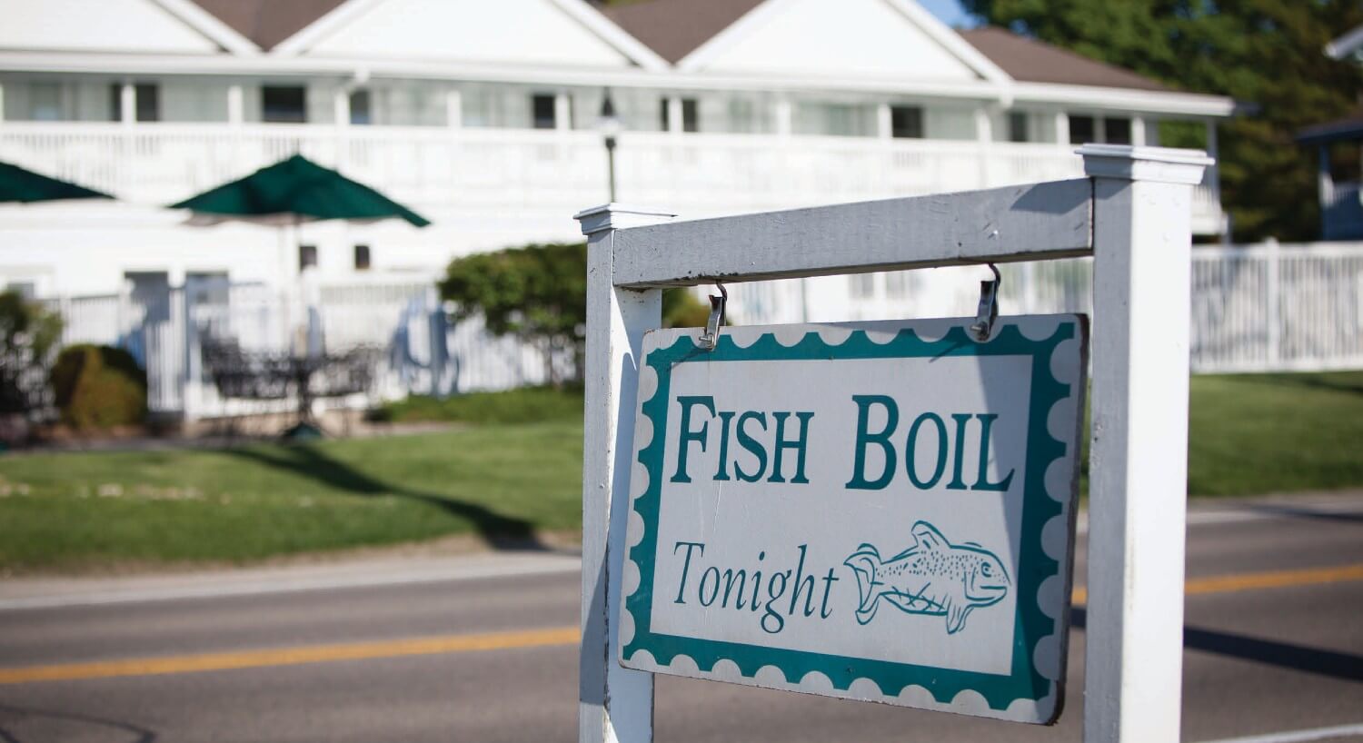 White and blue square sign on the side of the road advertising a fish boil