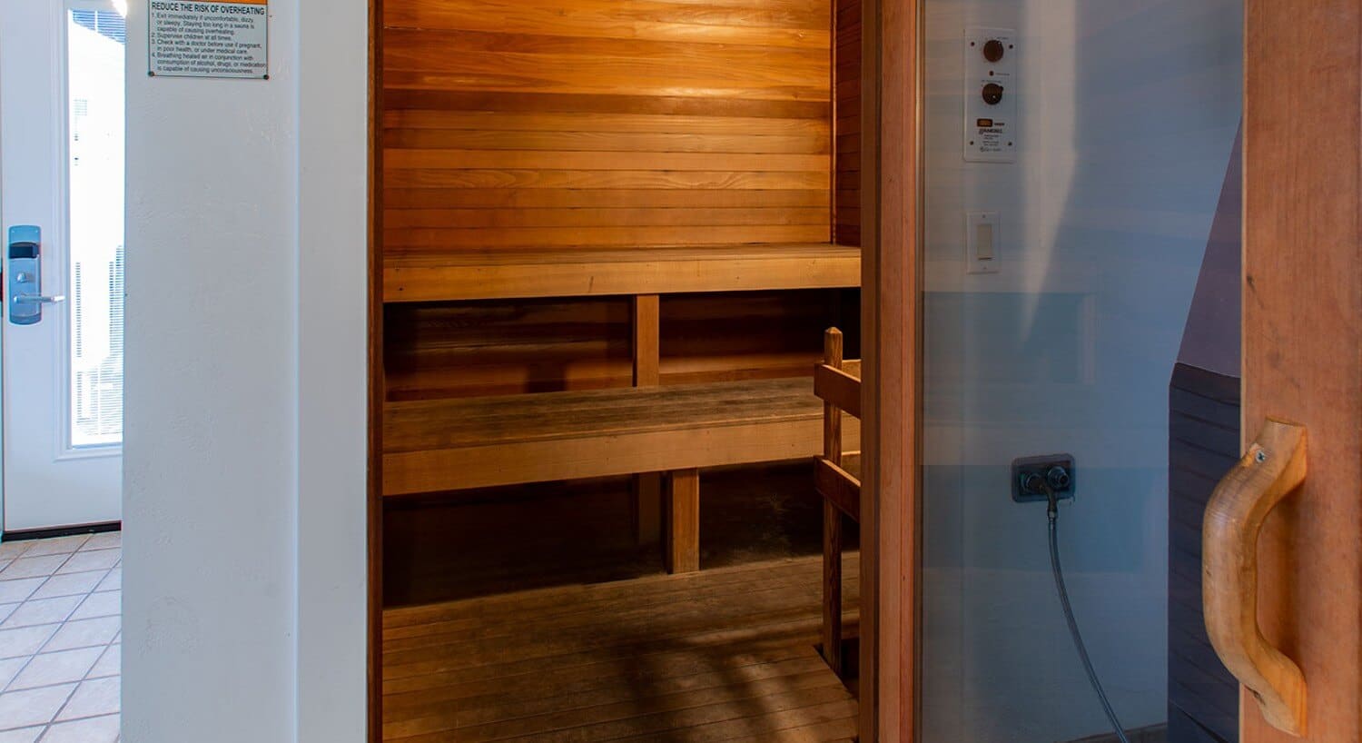Glass door open to a sauna with wood walls and two bench seats