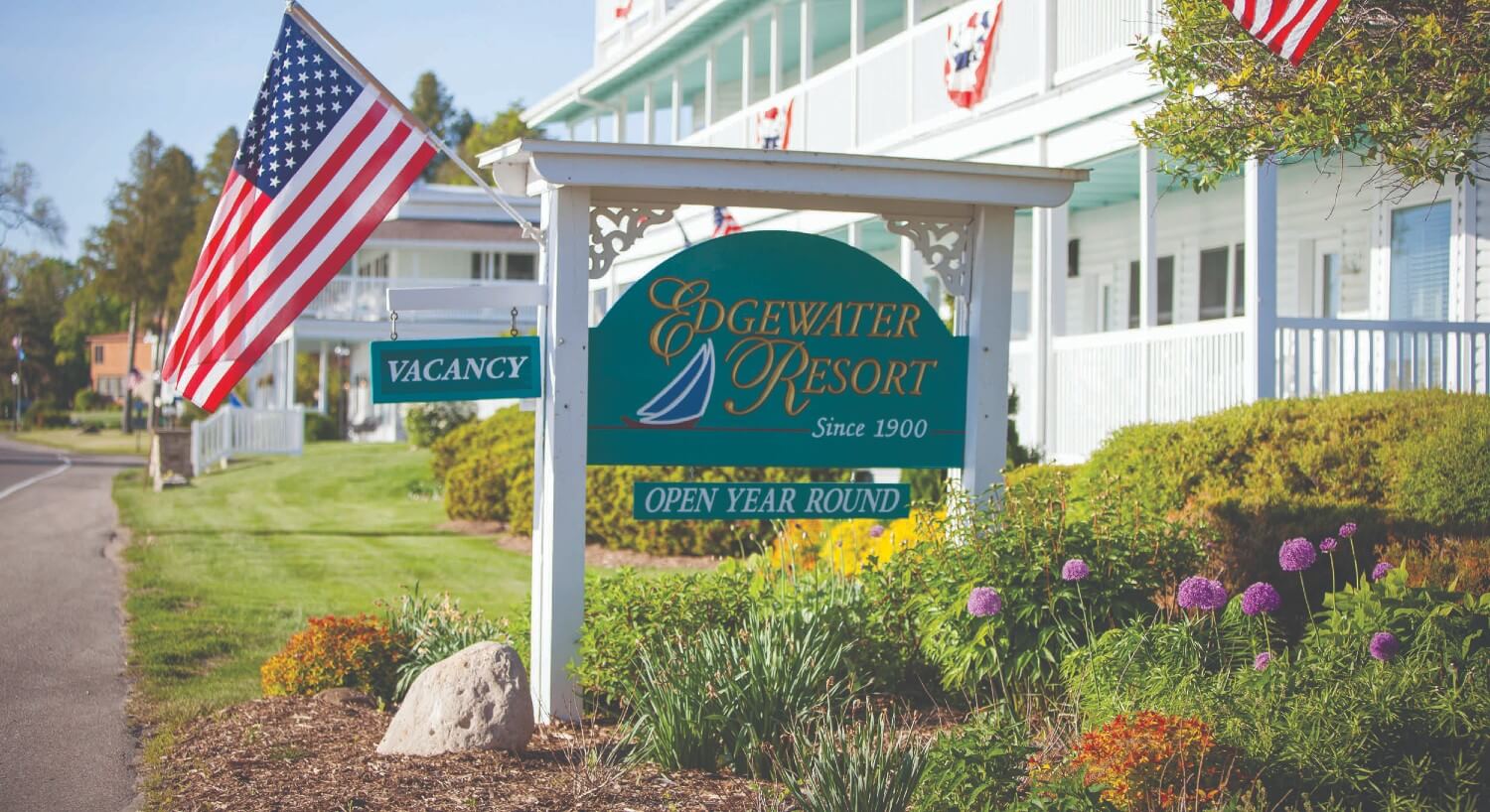 Large green and white business sign with gold text and a blue sailboat with an American flag on a small pole next to white hotel building