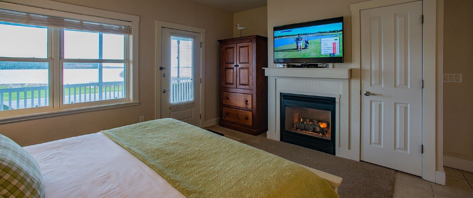 Bedroom with queen bed, large windows and door overlooking water, and TV over a gas fireplace