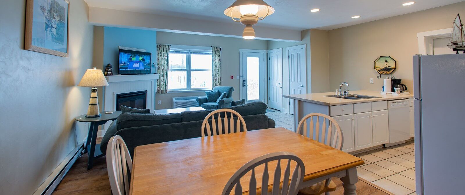 Suite with kitchenette, table with four chairs, living area with couch, chair, and TV over fireplace