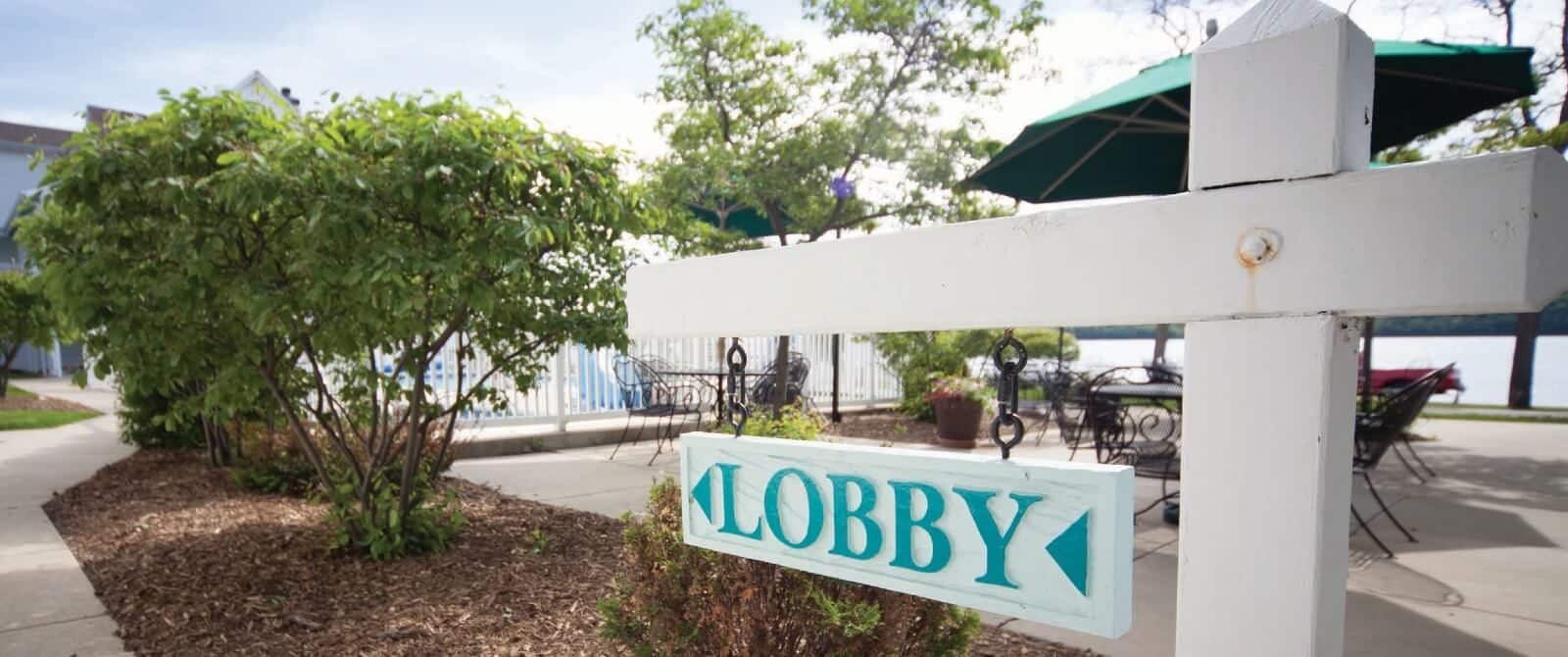 White sign pointing to a lobby next to shrubs and an outdoor patio table