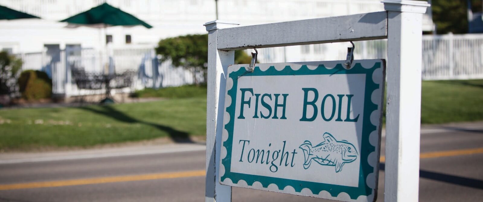 Blue and white sign next to a two lane road advertising a fish boil