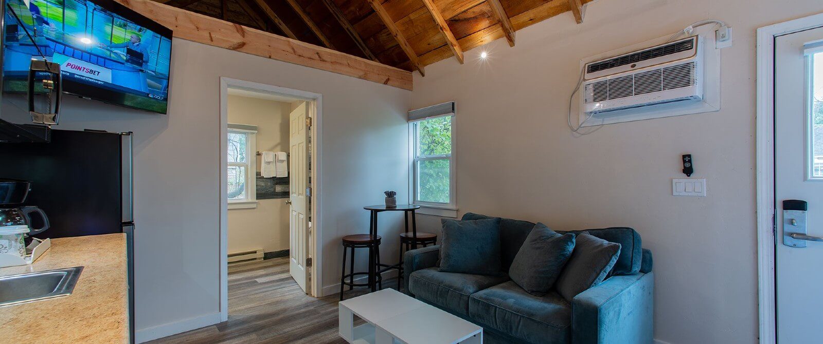 Interior of a cottage with plush couch, table and kitchenette, corner TV and doorway into a bathroom