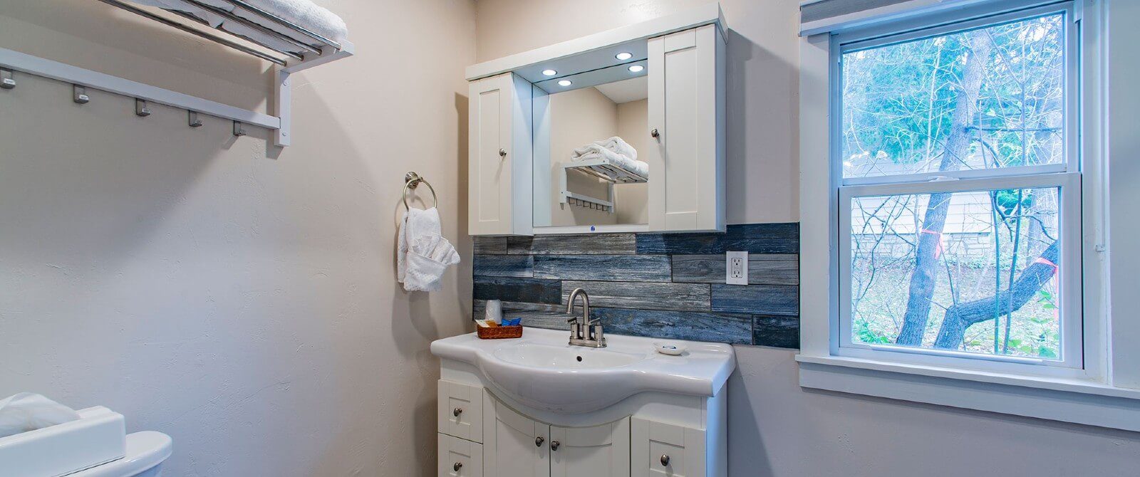 Small white bathroom with single sink vanity, mirror with side cabinets and large picture window