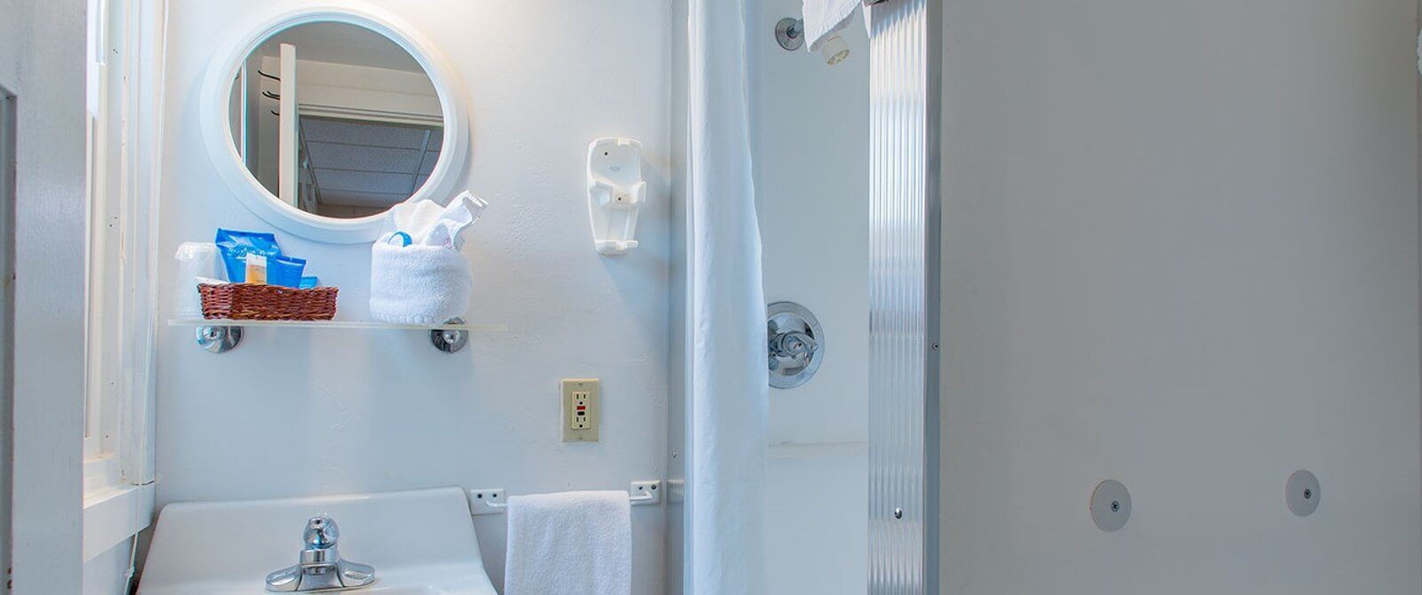 White bathroom with single sink, round framed mirror and stand up shower with white shower curtain