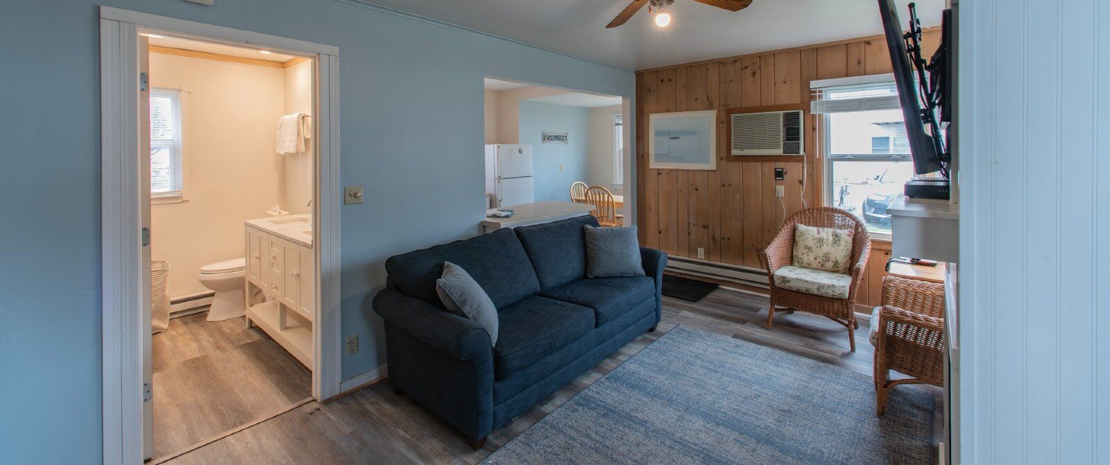 Interior of a cottage with couch, wicker sitting chairs, kitchen and doorway into a bathroom