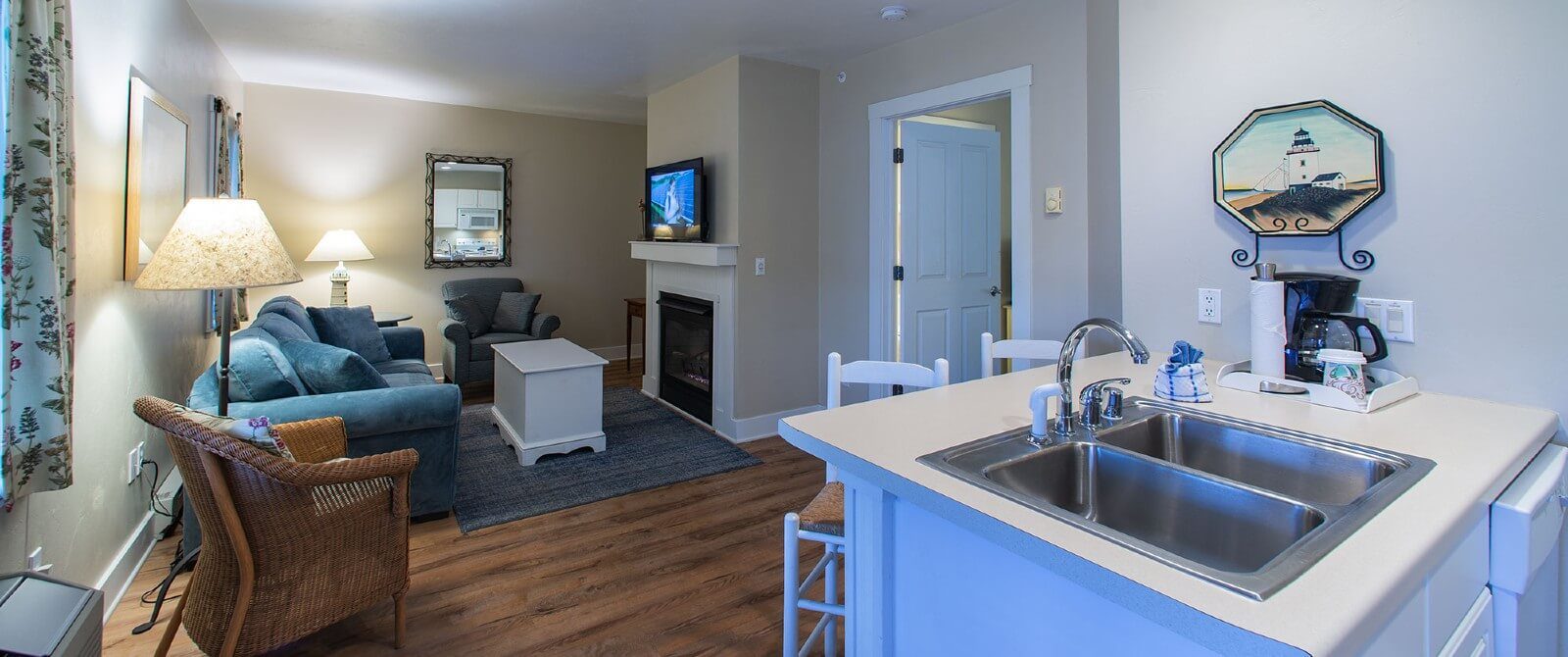 Suite with a small kitchen, living room with couch and chair in front of gas fireplace and doorway into a bedroom