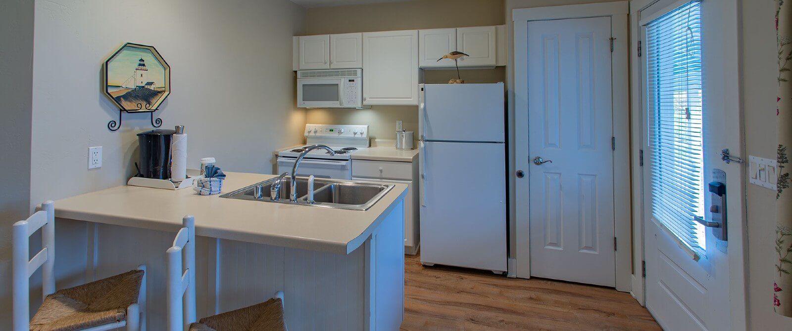 Small white kitchenette with hardwood floors and sink island with two stools