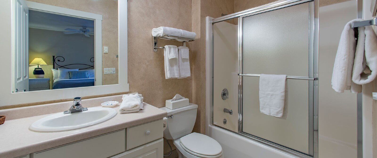 Bathroom with single sink vanity, white framed mirror, large shower with slider doors and white towels