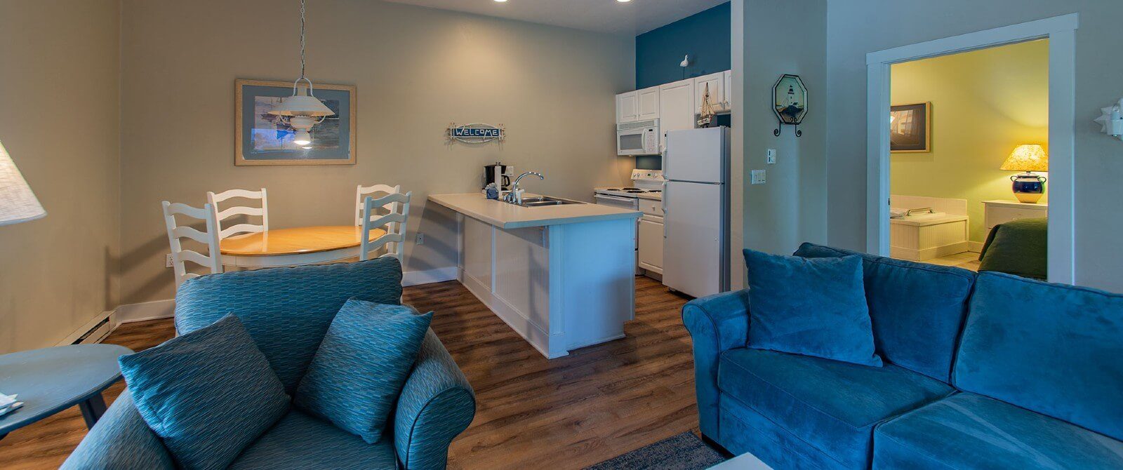 Suite with kitchen, hardwood floors, round table with four chairs, couch and chair and doorway into a bedroom with jacuzzi tub