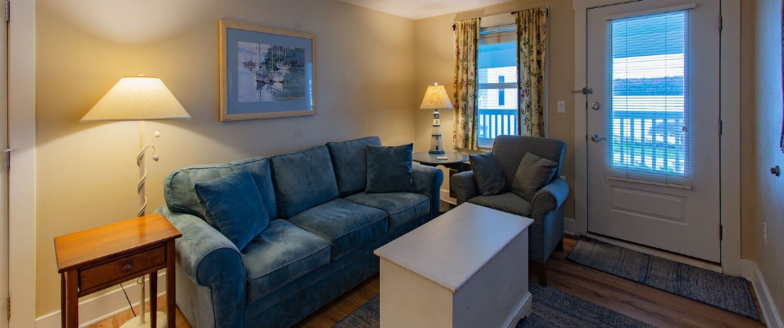 Living room with plush blue couch and chair, white coffee table next to a window and a door to the outside.