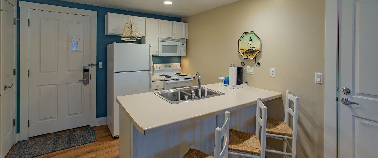 Small kitchenette with white cabinets, island counter with sink and three stools