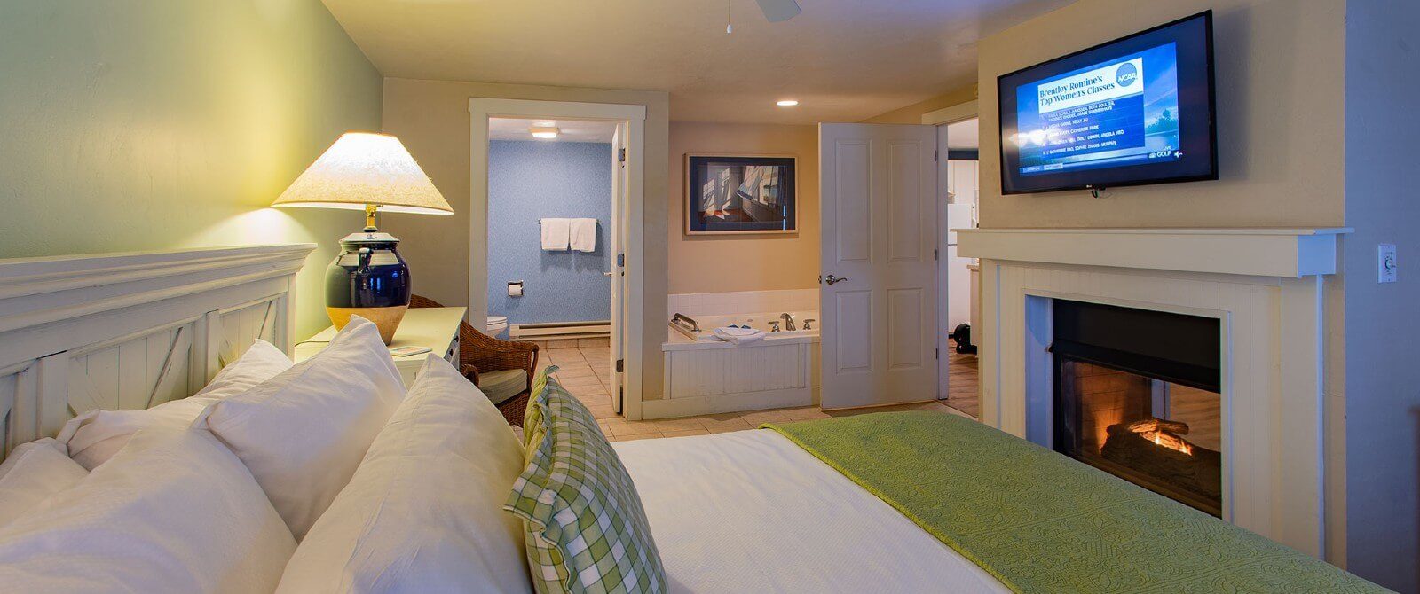Spacious bedroom with king bed in front of a gas fireplace, TV above and jacuzzi tub in corner