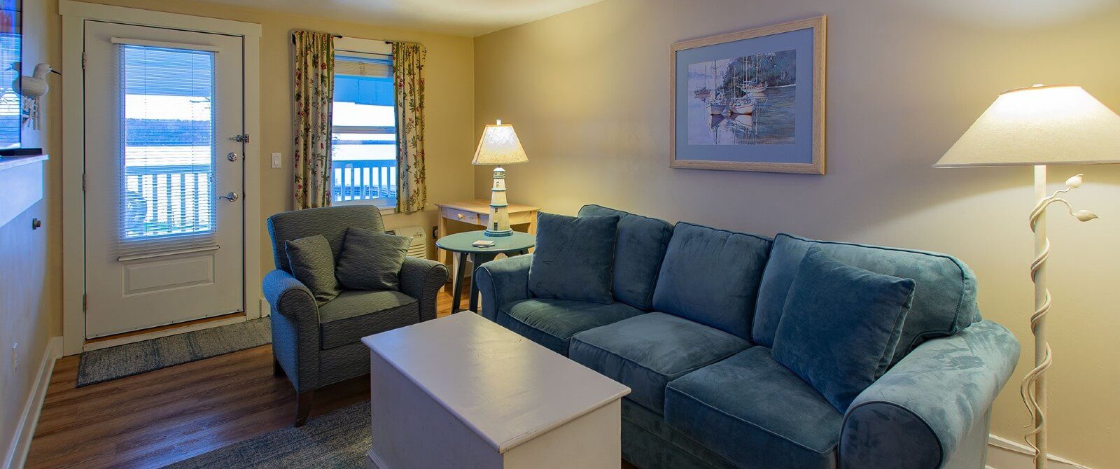 Living room with blue couch and chair coffee table, two lamps and large window next to a door