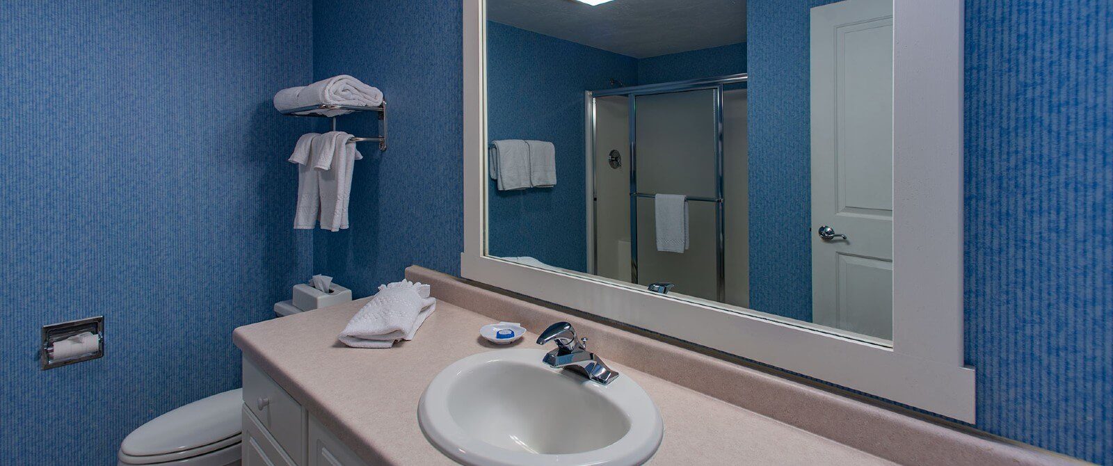 Bathroom with blue wallpaper, single sink vanity, toilet, white framed mirror and hanging towels