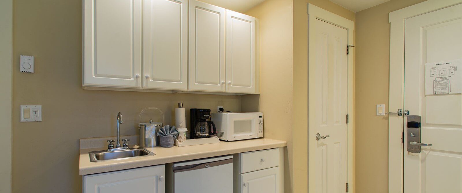 White kitchenette with upper and lower cabinets, sink, microwave and coffee maker