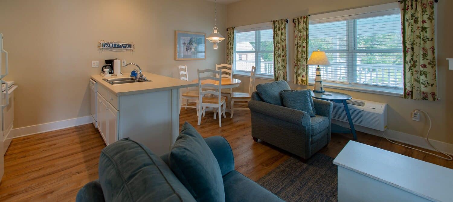 Hotel suite with kitchen, table with four chairs, living room with couch and chair and hardwood floors throughout