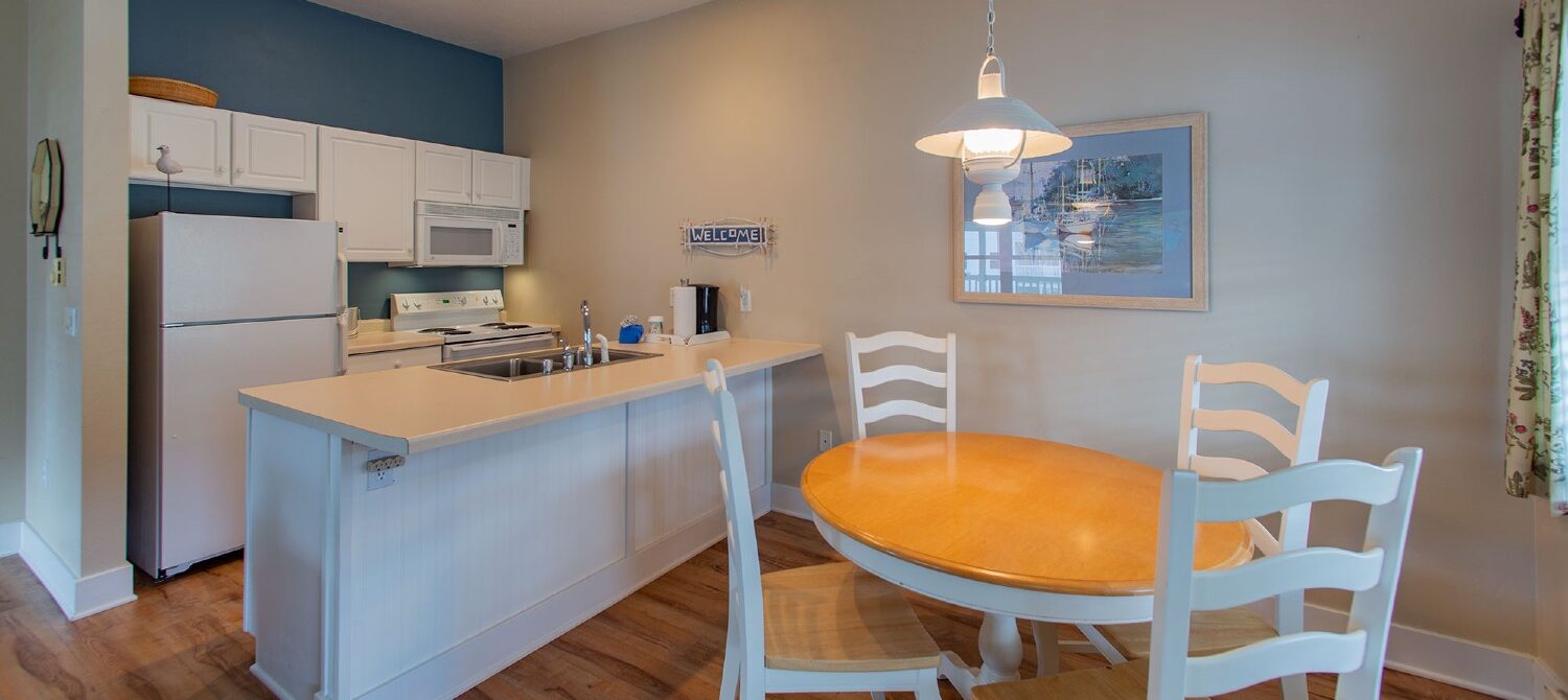 Kitchen of hotel suite with white cabinets, table with four chairs and hardwood floors