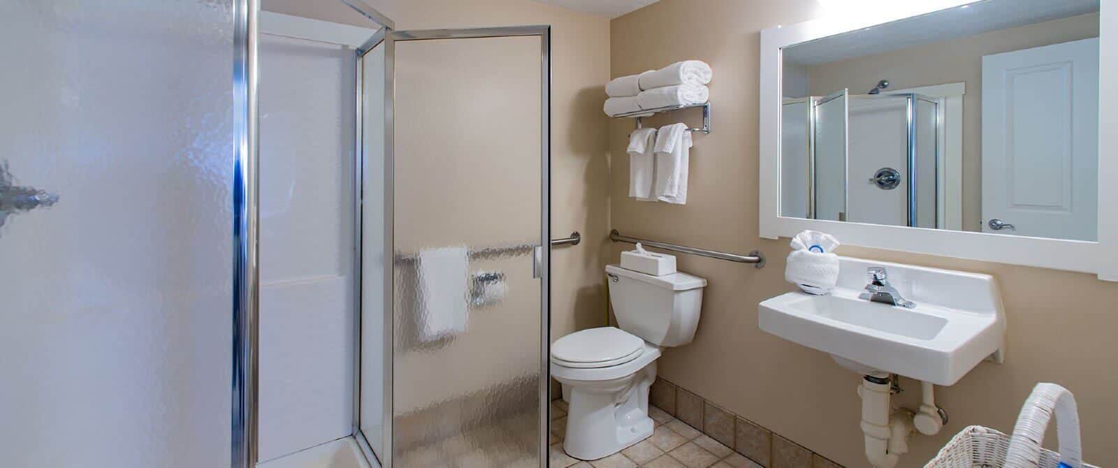 Bathroom with single sink, large framed mirror, toilet, plush white towels and stand up shower with glass doors