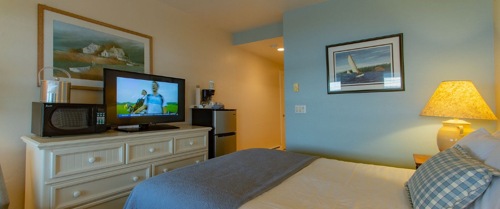 Bedroom with queen bed, dresser wth TV and microwave and small fridge