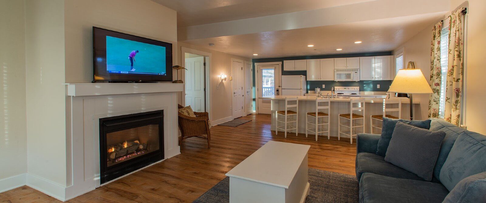 Spacious suite with kitchen, four stools, couch and coffee table in front of gas fireplace with TV on the mantle