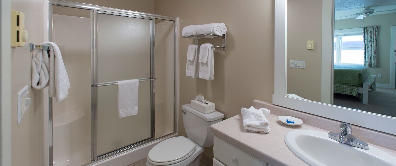 Bathroom with cream walls, stand up shower with slider door, sink with framed mirror and hanging towels