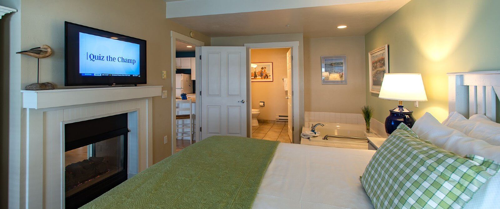 Spacious bedroom in hues of green and white, bed in front of two-sided gas fireplace, corner jacuzzi