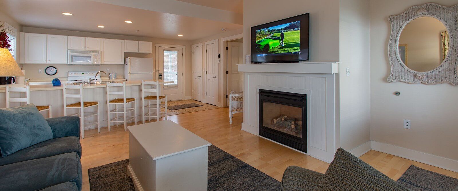 Suite with white kitchen, hardwood floors, couch and chair in front of gas fireplace with TV on the mantle