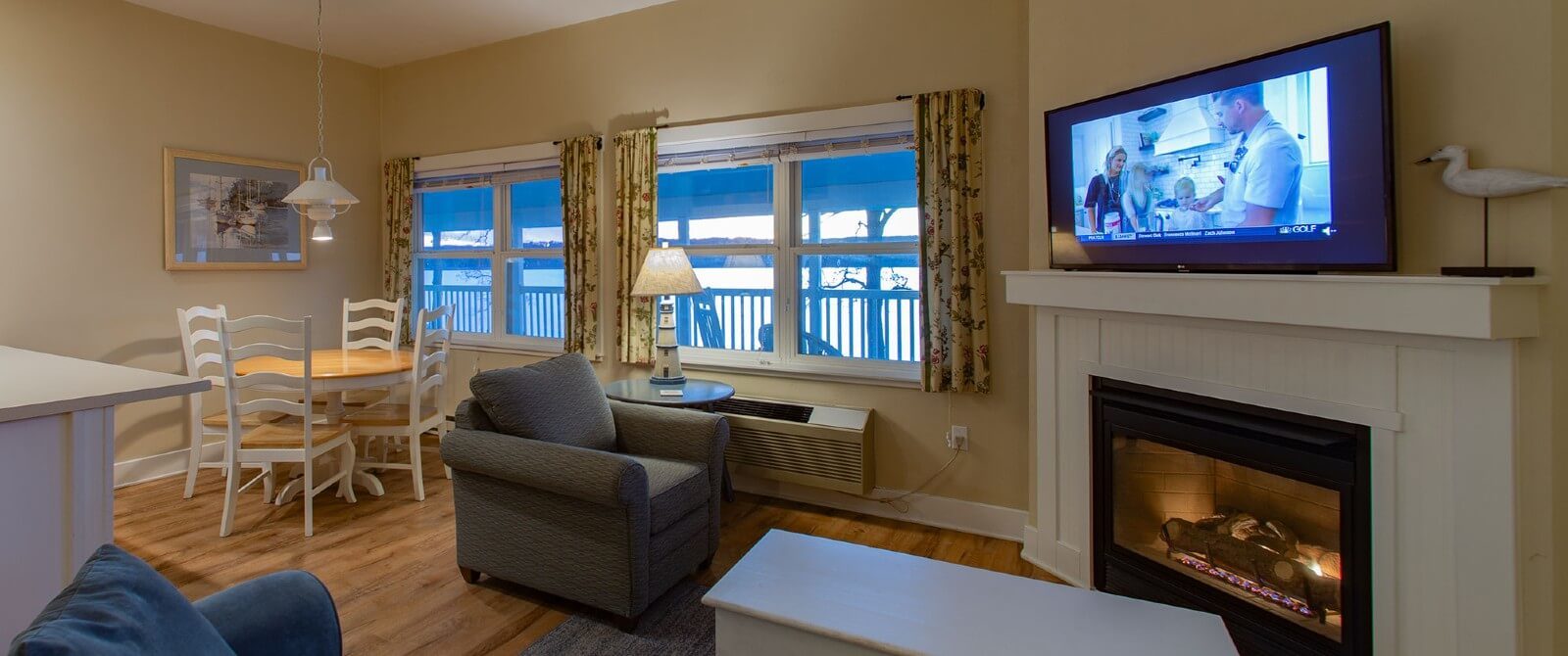 Cozy hotel suite with kitchenette, table with four chairs and couch and chair by a gas fireplace and large windows