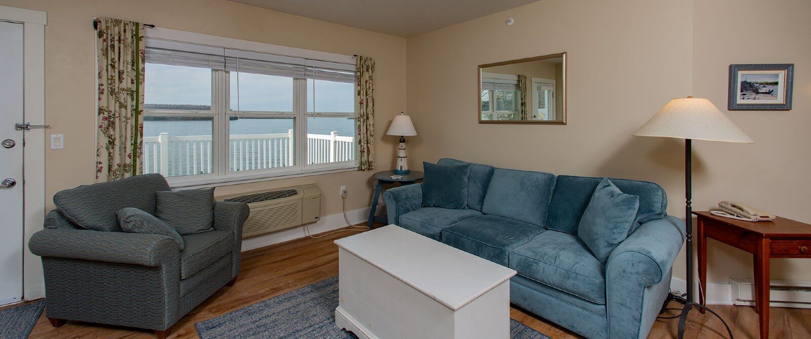 Living room with plush blue couch, chair, coffee table and large window overlooking the water