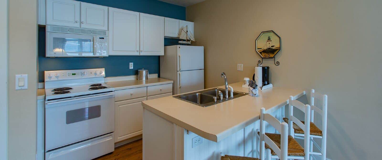 Small kitchen with hardwood floors, white cabinets and sink island with three white and brown stools