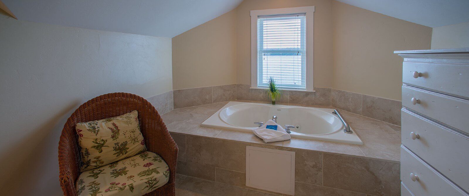 Large jacuzzi tub surrounded by tile under a window with blinds