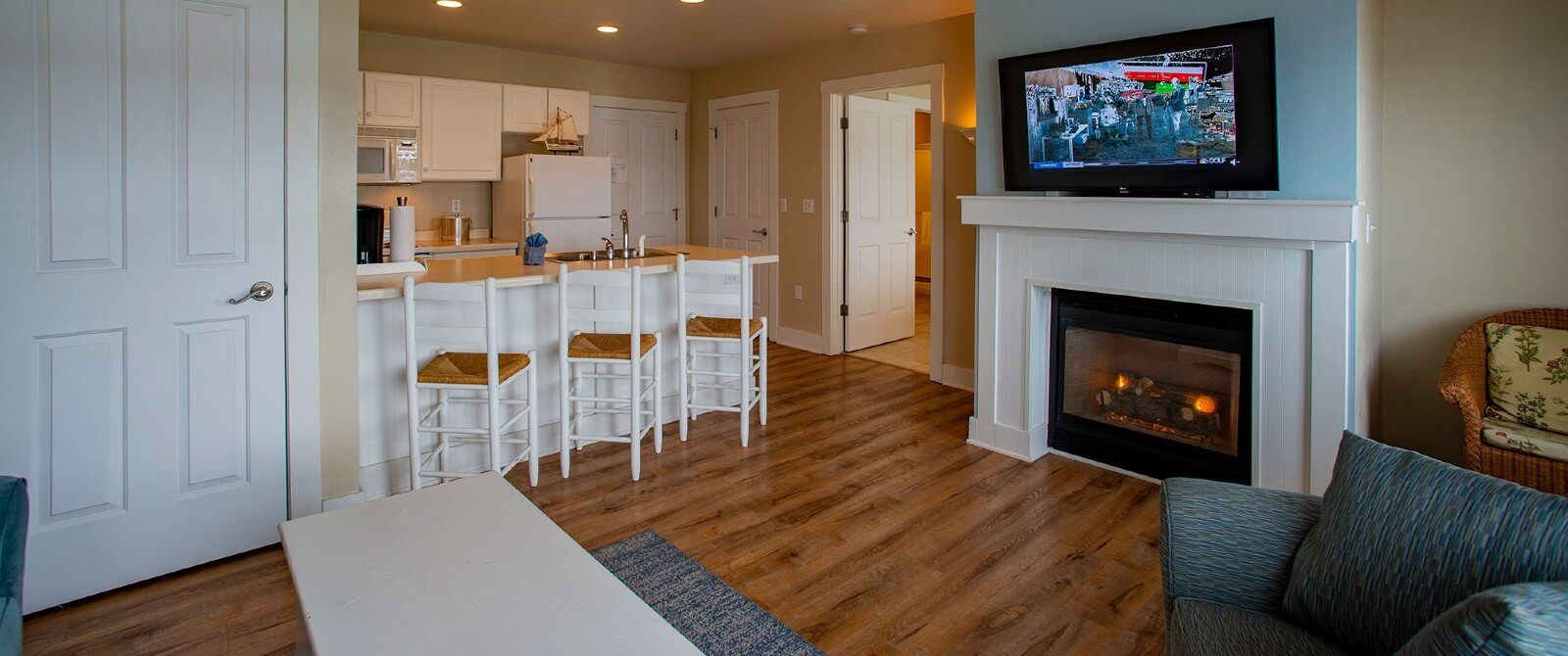 Hotel suite with kitchenette, hardwood floors, gas fireplace with TV on mantle and doorway into a bedroom