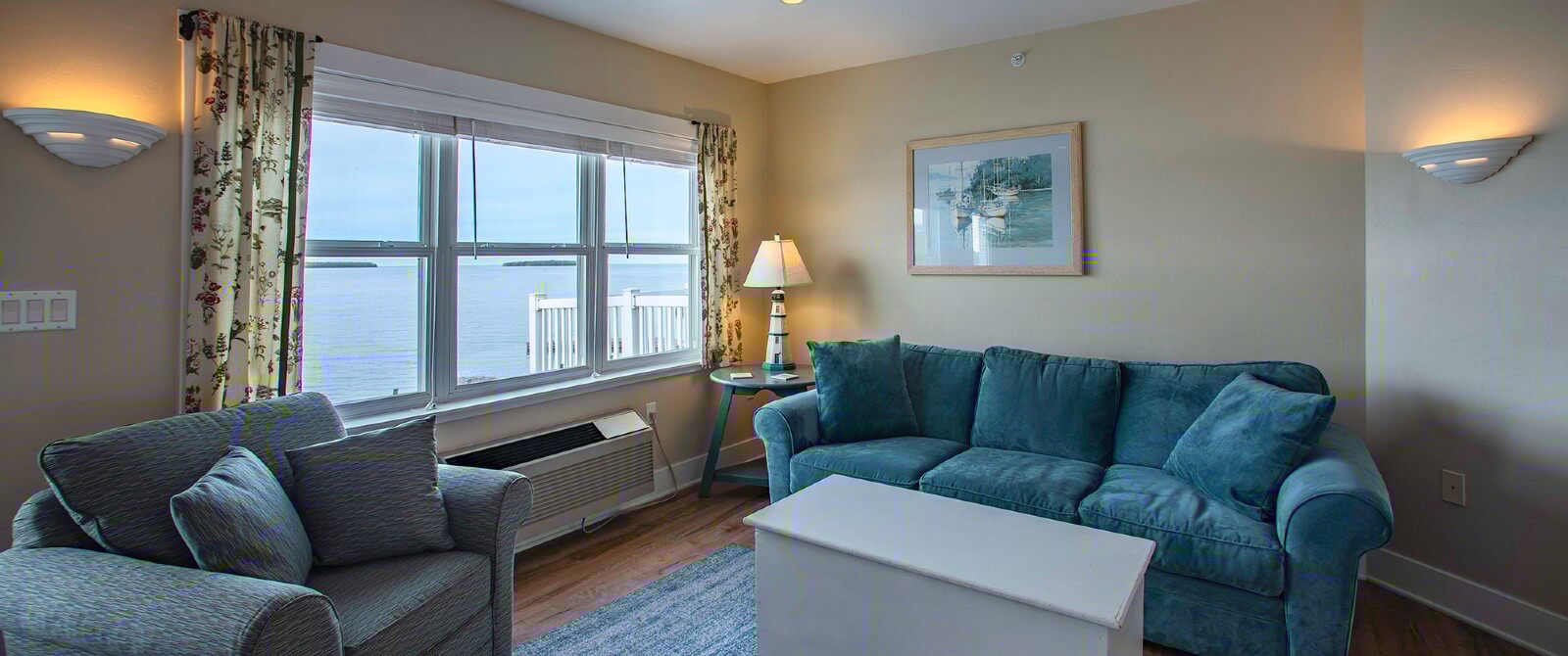 Living room with plush blue couch, chair, coffee table and large window overlooking the water