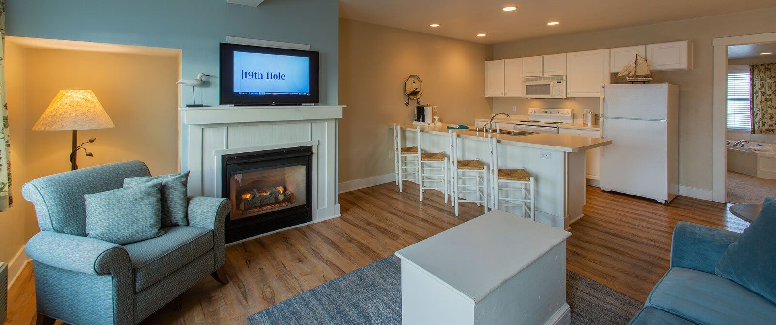 Suite showing living room with couch, chair, TV, and fireplace, kitchenette and open doorway to a jacuzzi tub