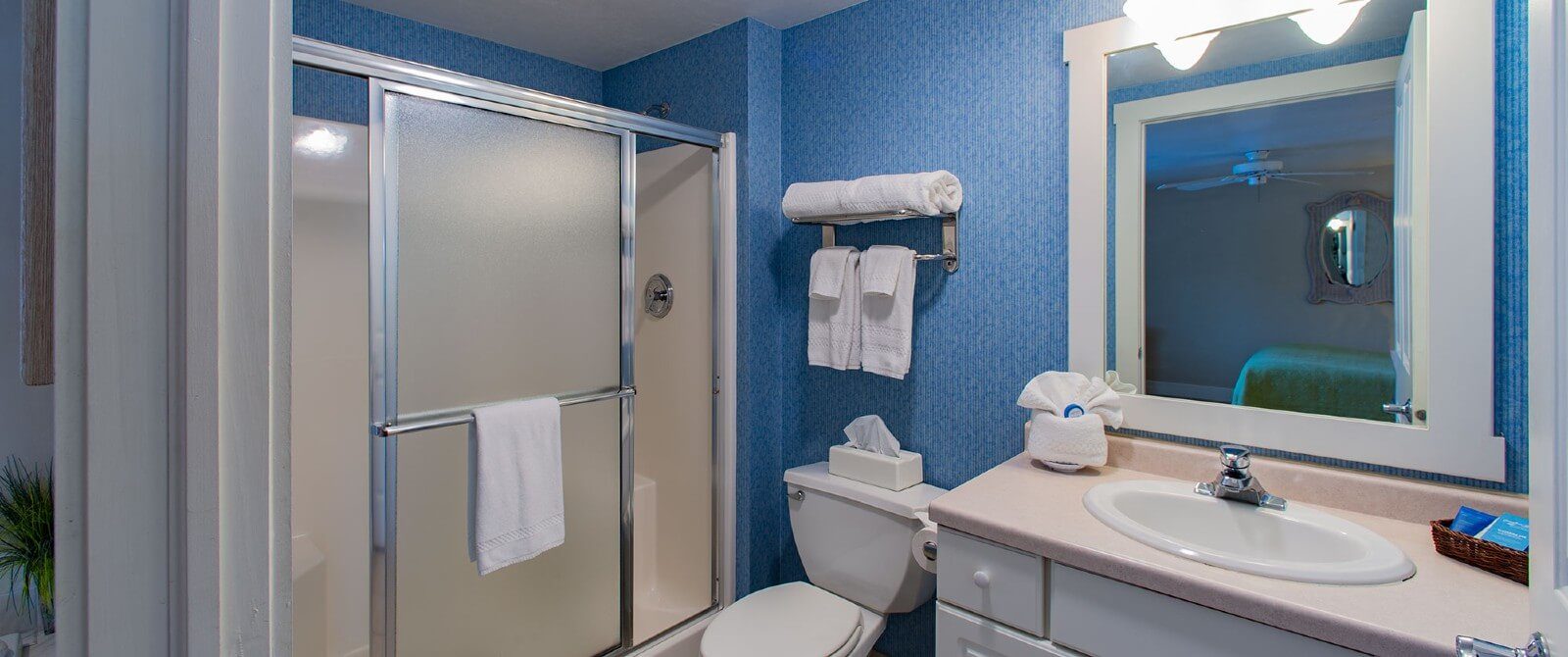 Bathroom with blue walls, shower with sliding doors, toilet and vanity with framed mirror