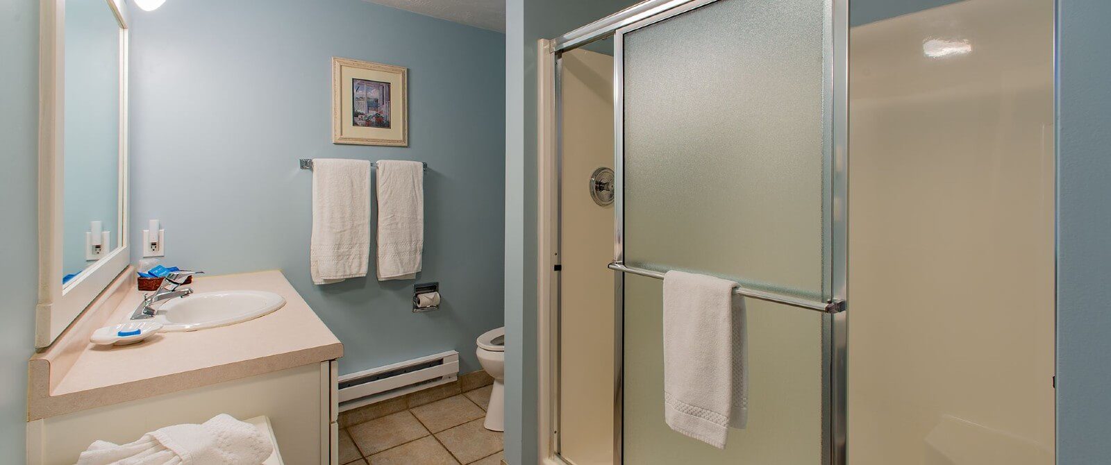 Bathroom with shower with sliding glass doors, sink, toilet, large framed mirror and hanging white towels