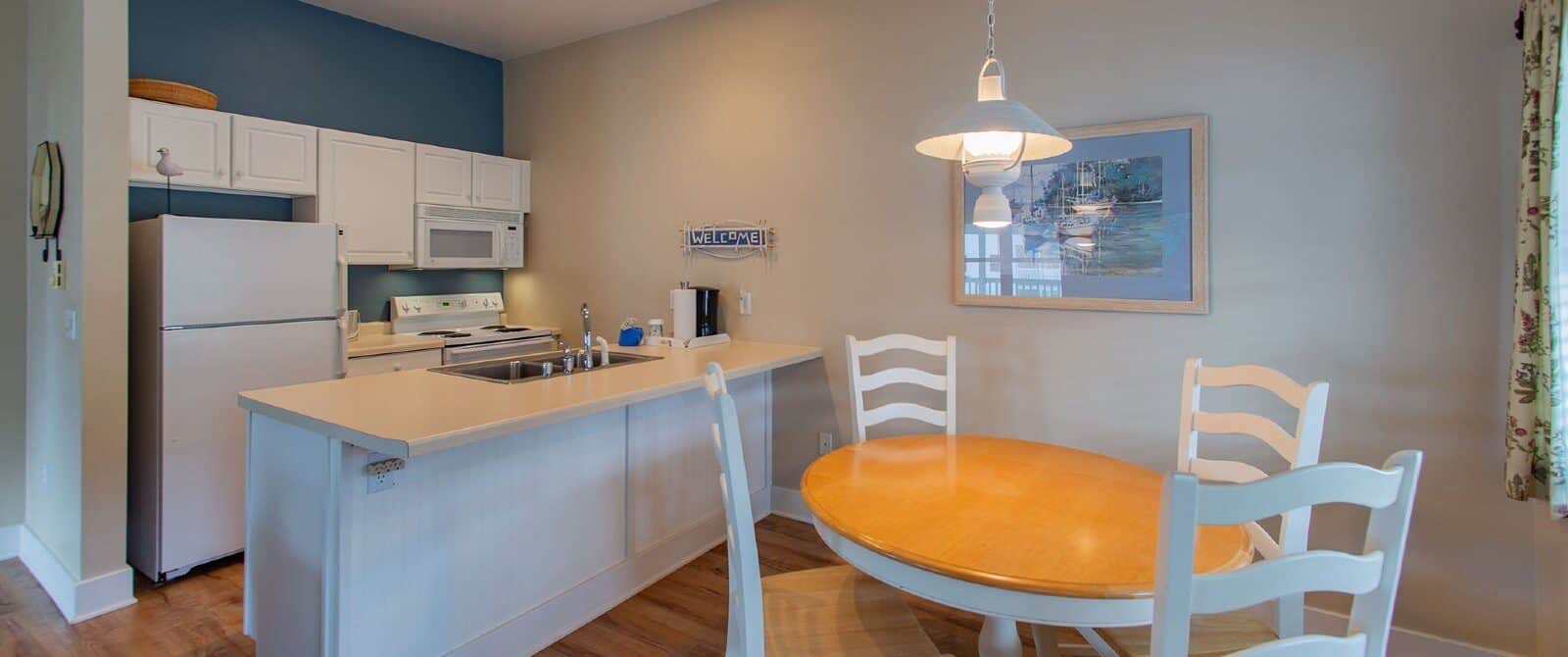 Small kitchen with white cabinets, round wood table with four white chairs