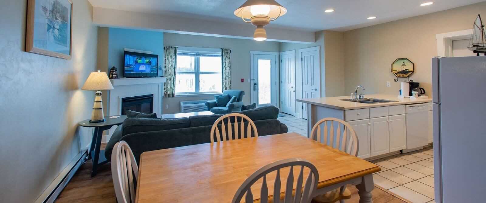 Large hotel suite with full kitchen, table with four chairs, living room with couch and chair and large window with curtains