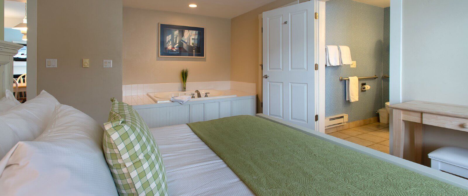 Elegant bedroom with king bed in green and white linens, soaker tub and doorway into a bathroom