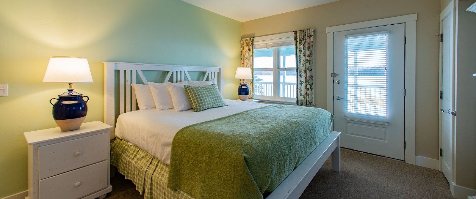 Bright bedroom with queen bed, side tables with lamps and window and door overlooking the water