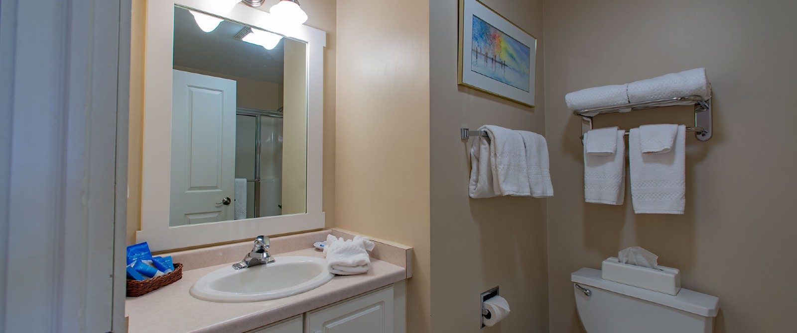 Bathroom with tan walls, sink with large white framed mirror and racks with white folded towels
