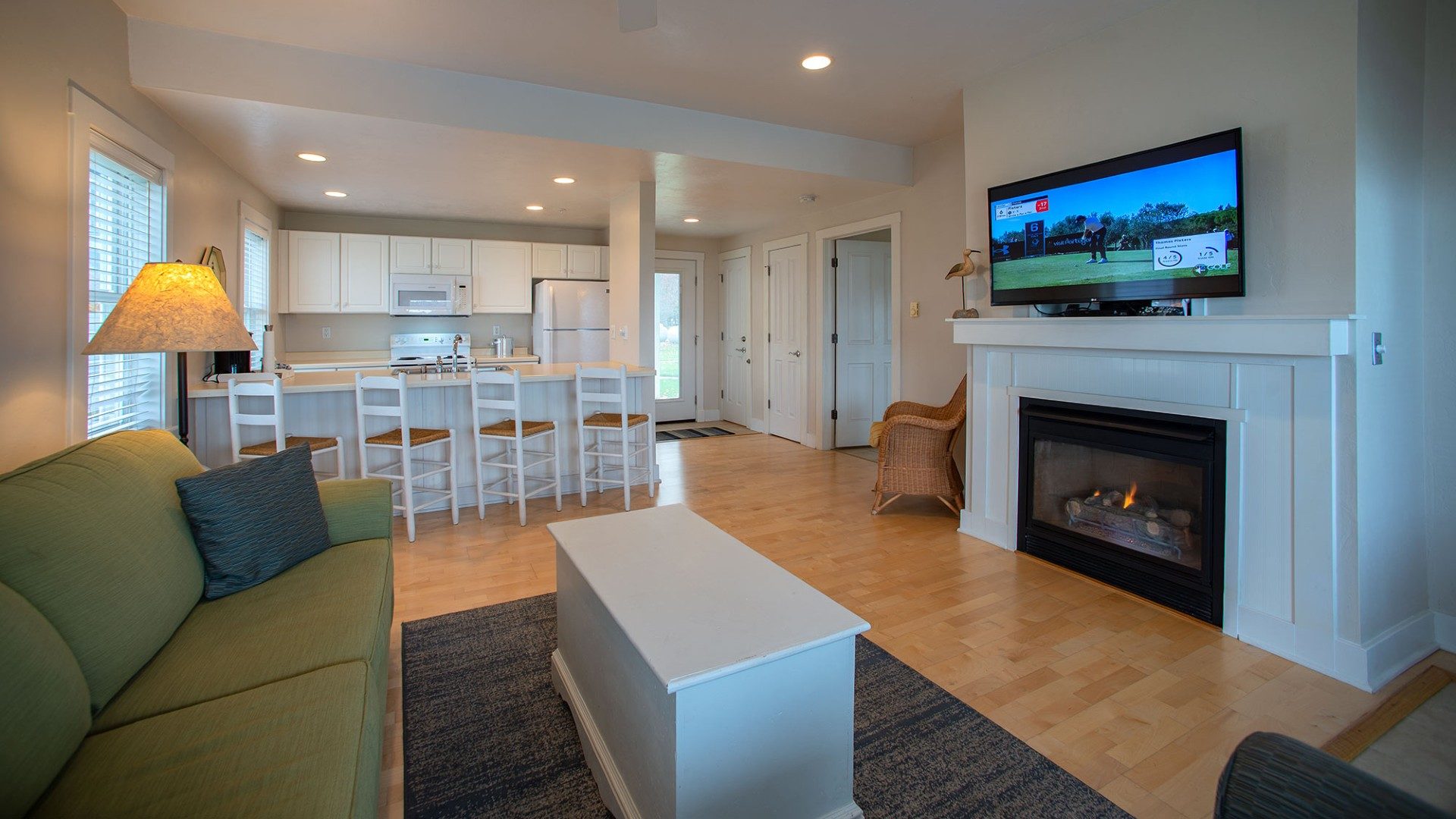 Suite showing a kitchen area, green couch with coffee table in front of a TV and fireplace