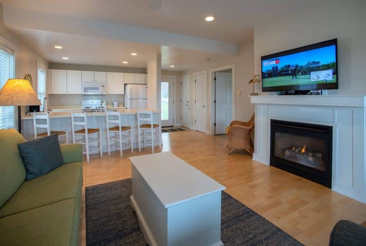 Suite showing a kitchen area, green couch with coffee table in front of a TV and fireplace